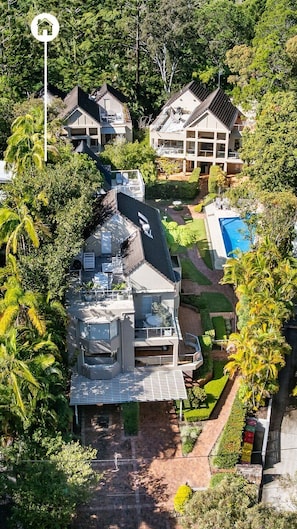 Une maison moderne à plusieurs étages, dotée d’une piscine et entourée d’une végétation luxuriante.