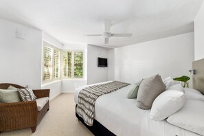 Une chambre à coucher avec un lit, un ventilateur de plafond, une télévision et une fenêtre avec des stores.