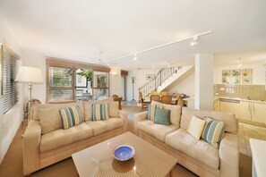 A spacious living room with two beige sofas, a coffee table, and a staircase leading to an upper level.
