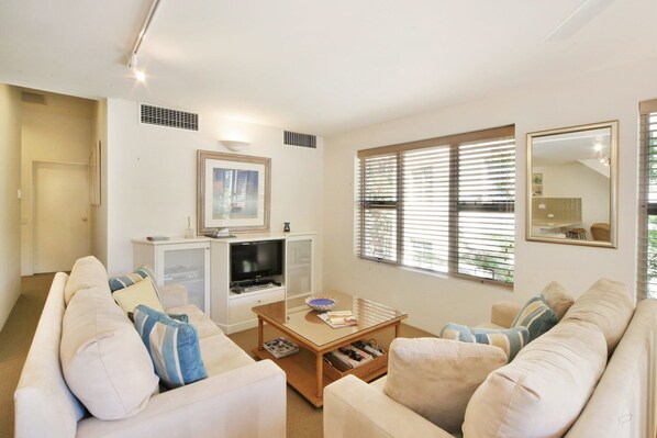 A living room with a sofa set, a coffee table, a television, and a window with blinds.