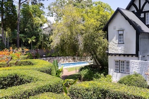 Una casa tradicional con piscina, rodeada de jardines cuidados y árboles.