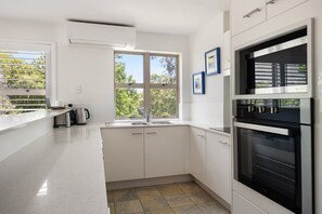 Eine moderne Küche mit weißen Schränken, einem Einbauofen und einem Fenster mit Blick auf Grünflächen.