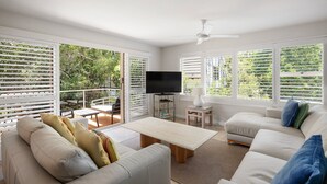 Un salon moderne avec un canapé, une table basse et un téléviseur. Il y a un balcon avec vue sur la verdure.