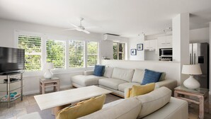 Un salon moderne avec un canapé d’angle, un téléviseur à écran plat et un ventilateur de plafond.