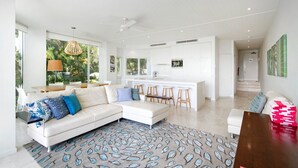 A modern living room with a white sofa, a dining area, and a kitchen with white cabinets. - Little Cove Apt - Spectacular View, Pool (Little Cove)
