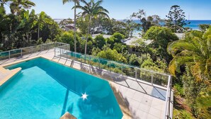 Une piscine dotée d’une barrière en verre, entourée d’une végétation tropicale et offrant une vue sur une étendue d’eau.