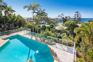 Une piscine dotée d’une barrière en verre, entourée d’une végétation tropicale et offrant une vue sur une étendue d’eau.