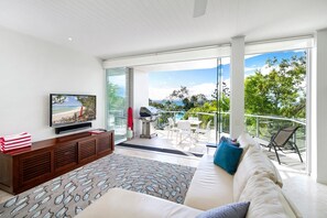 A modern living room with a television, a sofa, and a balcony with a view of the ocean. - Little Cove Apt - Spectacular View, Pool (Little Cove)