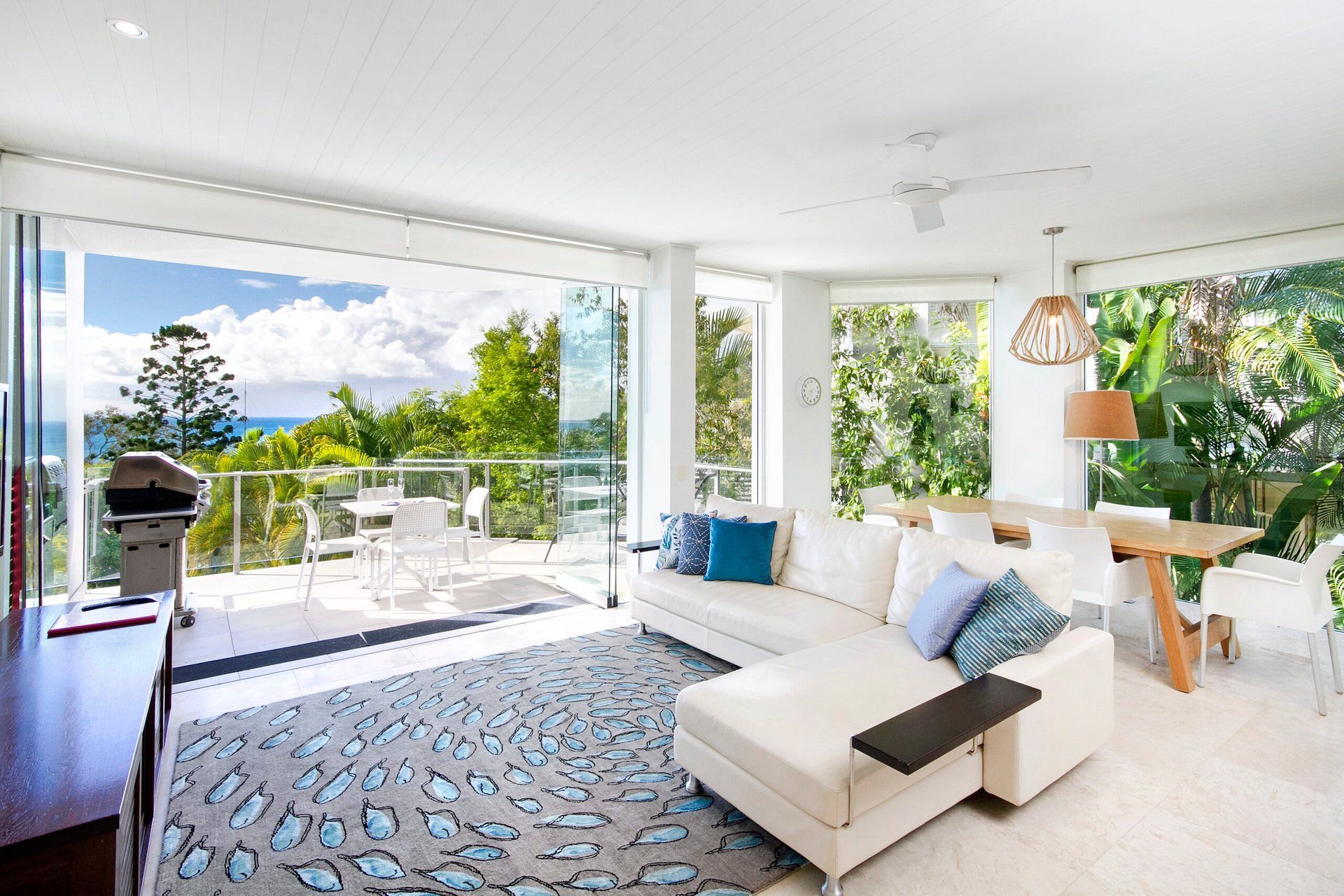 A modern living room with a sofa, a dining table, and a balcony with a grill.