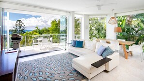 A modern living room with a sofa, a dining table, and a balcony with a grill. - Little Cove Apt - Spectacular View, Pool (Little Cove)