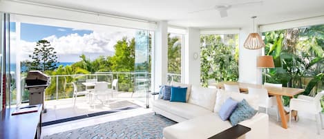 A modern living room with a sofa, a dining table, and a balcony with a grill.