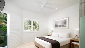 Une chambre à coucher avec un lit, un ventilateur de plafond, une fenêtre avec des stores et un tableau encadré au mur.