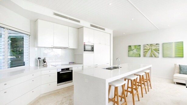A modern kitchen with white cabinetry, a built-in oven, and a large island with bar stools. - Little Cove Apt - Spectacular View, Pool (Little Cove)