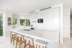A modern kitchen with a large island, white cabinetry, and bar stools. - Little Cove Apt - Spectacular View, Pool (Little Cove)