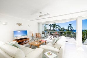 Un salon moderne doté d’un téléviseur à écran plat, de sièges confortables, d’un ventilateur de plafond et d’un balcon offrant une vue sur la plage.