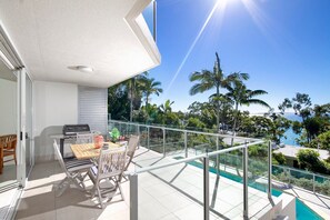 Un balcon avec une table et des chaises, donnant sur une piscine et des palmiers.