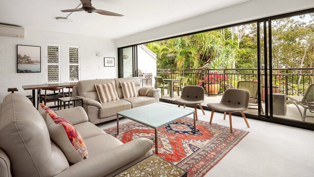 A modern living room with a sofa, chairs, a coffee table, and a large window offering a view of greenery. - Bayona 2 - Family Beach Charm (Little Cove)