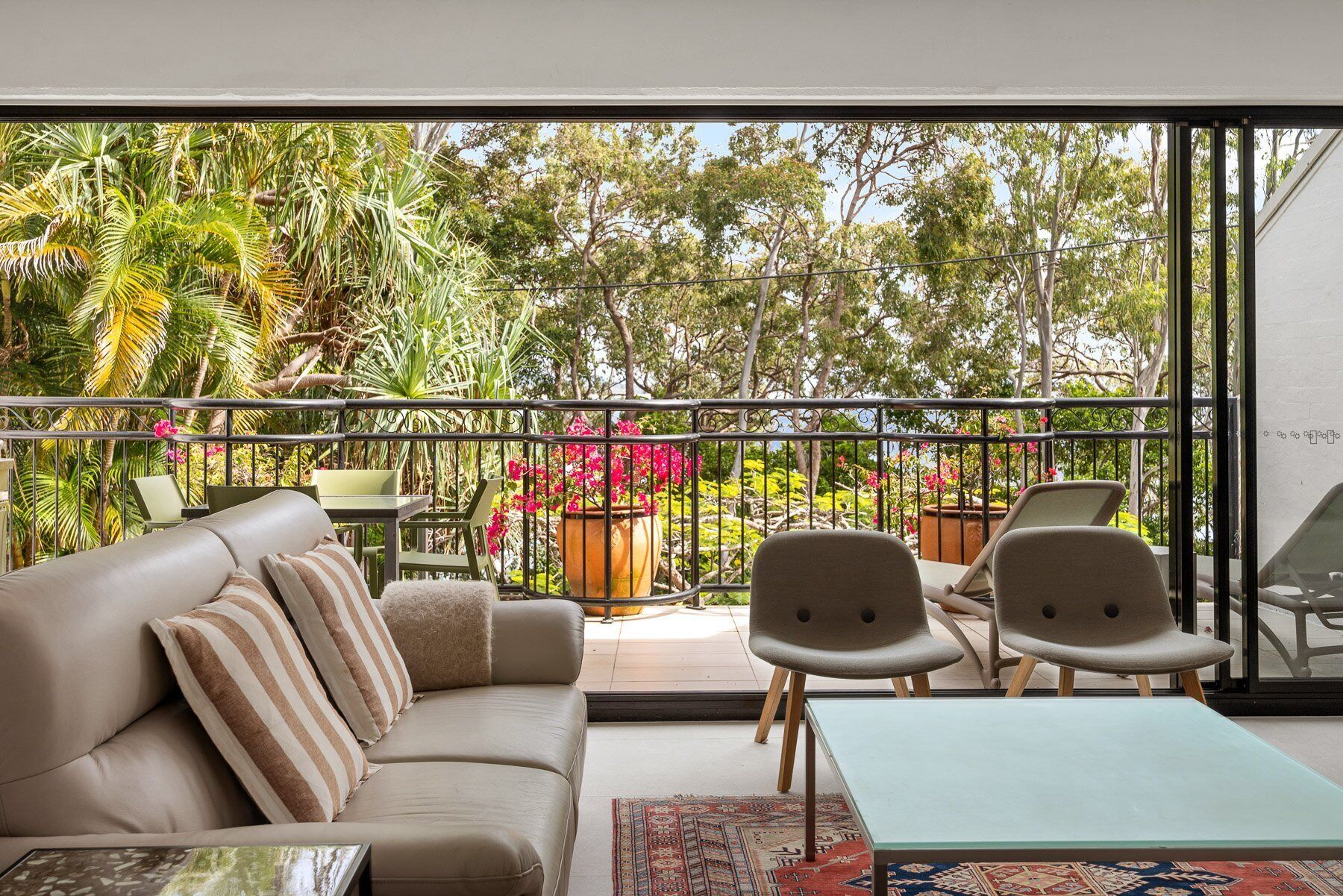 Una sala de estar moderna con sofá, sillas y una mesa, con vistas a un jardín exuberante y árboles.
