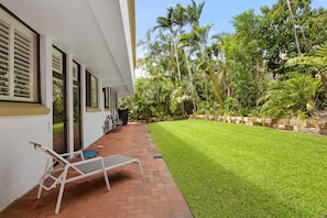 Une maison dotée d’une terrasse dallée, d’une pelouse et de diverses plantes tropicales.