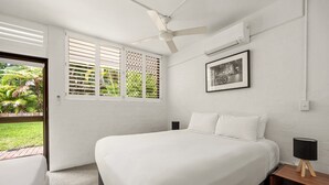 A bedroom with a bed, a nightstand, a ceiling fan, an air conditioning unit, and a window with a view of greenery. - Bayona 2 - Family Beach Charm (Little Cove)