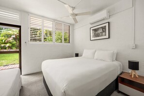 A bedroom with a bed, a nightstand, a ceiling fan, an air conditioning unit, and a window with a view of greenery. - Bayona 2 - Family Beach Charm (Little Cove)
