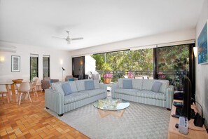 A modern living room with a glass coffee table, striped sofas, and a view of greenery through large windows. - Bayona 4 - Balcony Tranquility (Little Cove)