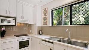 A modern kitchen with white cabinets, a built-in microwave, a stove, a dishwasher, and a large window with a view of greenery. - Bayona 4 - Balcony Tranquility (Little Cove)