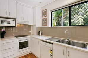 A modern kitchen with white cabinets, a built-in microwave, a stove, a dishwasher, and a large window with a view of greenery. - Bayona 4 - Balcony Tranquility (Little Cove)