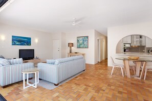 A modern living room with a sofa, a television, and a dining area with a table and chairs. - Bayona 4 - Balcony Tranquility (Little Cove)