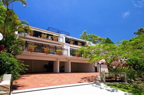 Un immeuble à plusieurs étages doté de balcons, de plantes en pot et d’un espace d’entrée pavé.