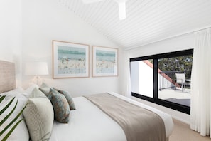 A bedroom with a bed, pillows, a nightstand, a lamp, and two framed beach paintings on the wall.