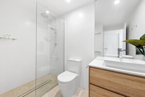 A modern bathroom with a glass-enclosed shower, a white toilet, and a wooden vanity with a sink.