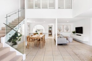 Ein modernes Interieur mit Treppe, Essbereich, Wohnbereich und einem an der Wand befestigten Fernseher.