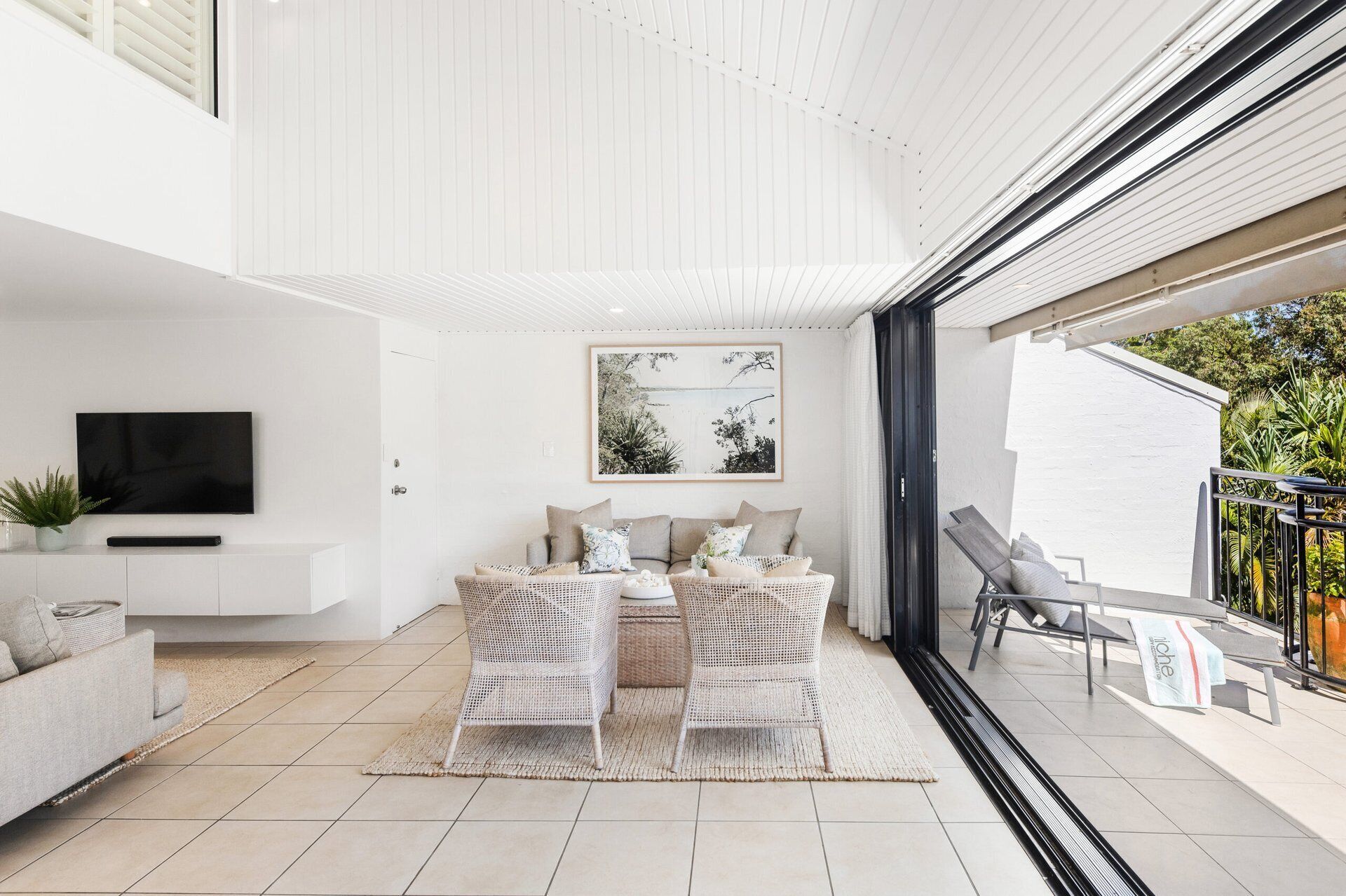 Un salon moderne doté d’un téléviseur à écran plat, d’un canapé, d’un coin repas avec une table et des chaises, et d’un balcon aménagé avec du mobilier d’extérieur.