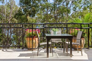 An outdoor patio with a table and chairs, surrounded by a metal railing, overlooking a forested area.