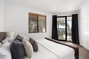A hotel room with a bed, a window with blinds, a balcony with a table and chairs, and a door.