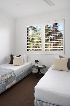 A hotel room with two beds, a small table, and a window with blinds.