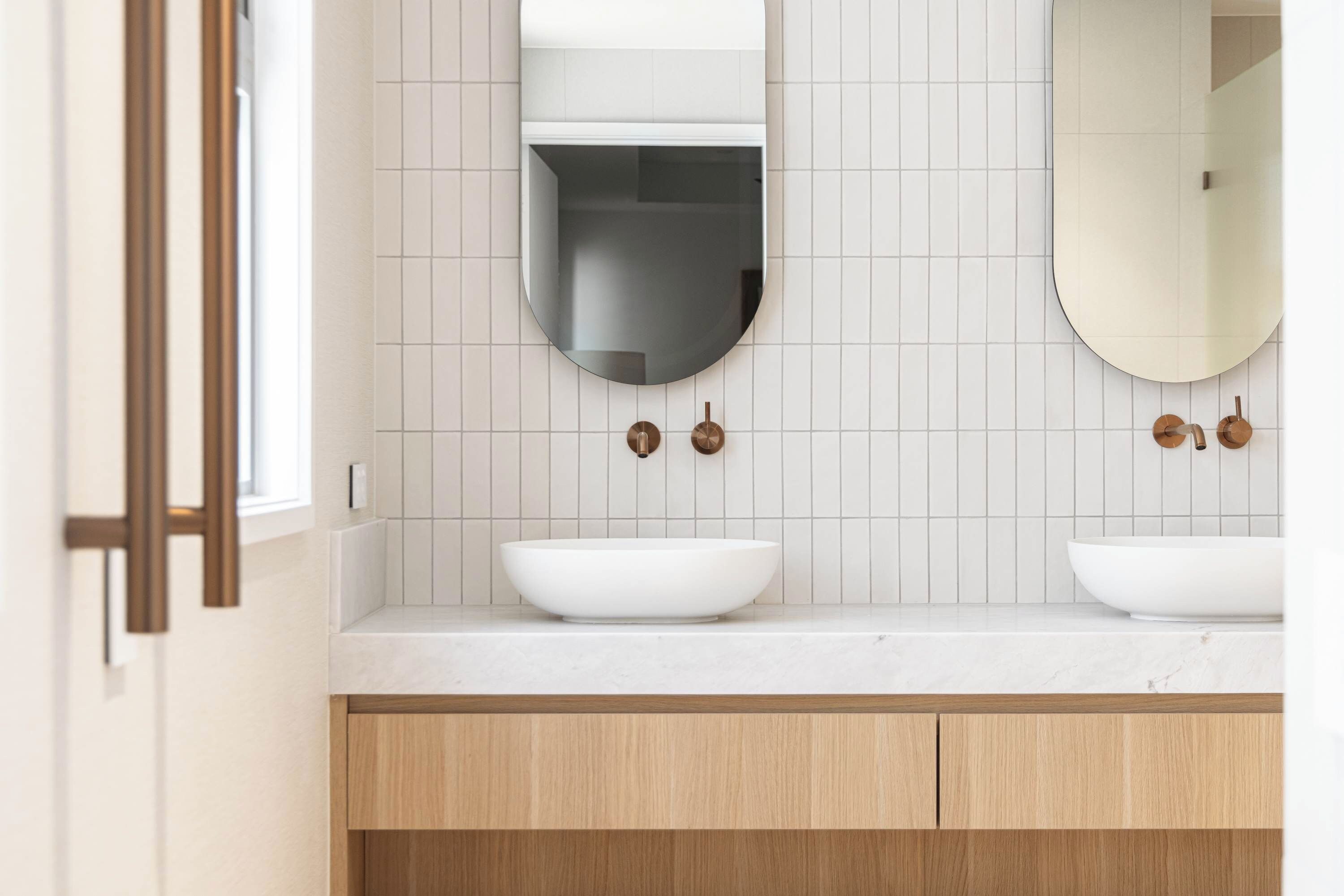 Une salle de bain avec deux lavabos blancs, un miroir au-dessus de chacun, et un meuble-lavabo en bois.