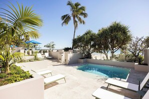 Ein Poolbereich mit Liegestühlen, Palmen und Blick auf den Strand.