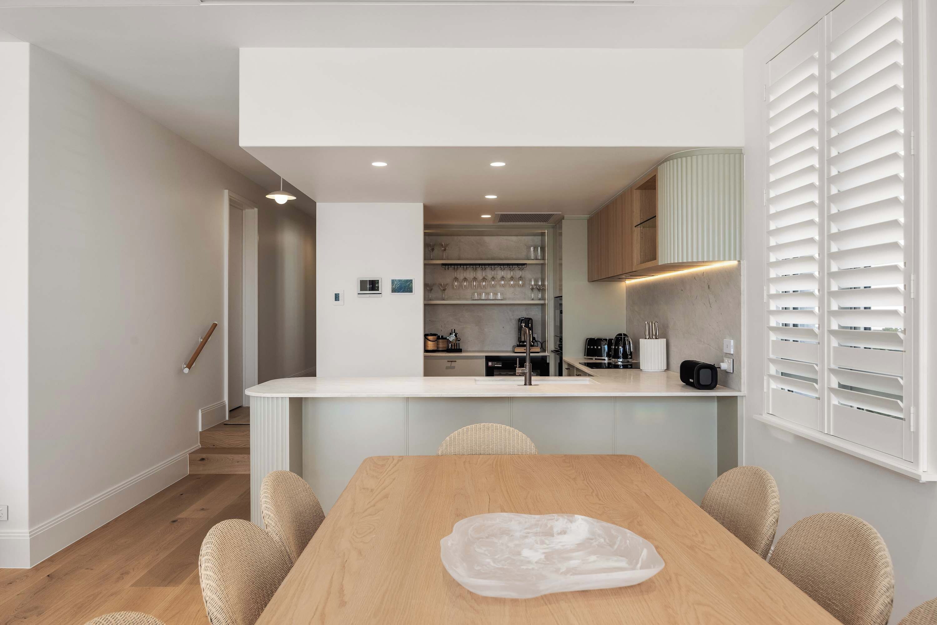 A modern kitchen with a central island, built-in appliances, and a dining area with a wooden table and wicker chairs.
