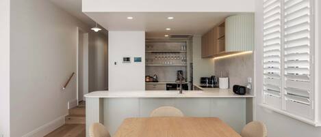 A modern kitchen with a central island, built-in appliances, and a dining area with a wooden table and wicker chairs.