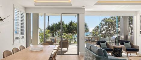 A modern living room with a large sliding glass door leading to an outdoor area with a view of palm trees and the sea.