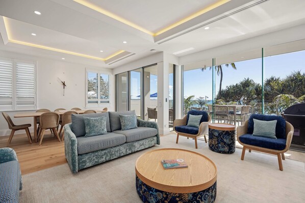 A modern living room with a sofa, chairs, a coffee table, and large windows offering a view of the outdoors.