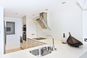 Enjoy cooking in this stylish kitchen with sleek cabinetry, a stainless steel sink, and a glass staircase.