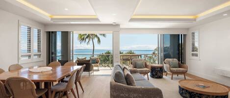 A spacious living area with a large wooden table, comfortable seating, and a view of the ocean.