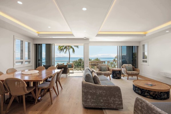 A spacious living area with a large wooden table, comfortable seating, and a view of the ocean.