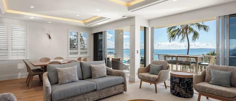 Ein modernes Wohnzimmer mit einer Couch, Sesseln, einem Couchtisch und Blick auf den Ozean.