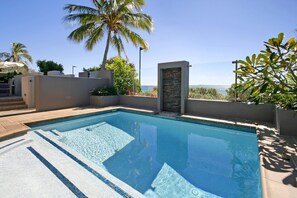 Relax by the pool surrounded by lush greenery and a palm tree.