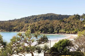 A beach with clear water, surrounded by dense forest and hills.