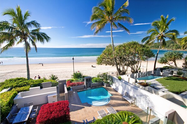 Relax by the pool surrounded by lush vegetation and palm trees, with a serene beach view.